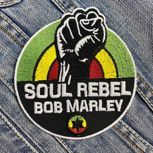 Könnte beinhalten: Schwarzer und weißer gestickter Aufnäher mit einer erhobenen Faust, einem Regenbogenbogen und dem Text "Soul Rebel Bob Marley".