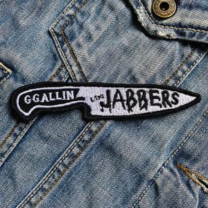 Könnte beinhalten: Ein gestickter Patch in Schwarzweiß in Form eines Messers mit dem Text "G'GALLIN'  'N' JABBERS" auf einem Jeansstoff-Hintergrund.
