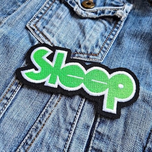 Puede incluir: Parche bordado verde y blanco con la palabra "Sleep" en una chaqueta vaquera.
