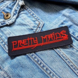 Może przedstawiać: Czarna łatka z wyhaftowanymi czerwonymi literami „Pretty Maids”. Łatka jest przyszyta do niebieskiej dżinsowej kurtki.