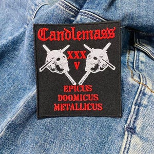 Może przedstawiać: Czarna łatka z białymi haftowanymi czaszkami i czerwonym tekstem, który brzmi "Candlemass", "XXXV", "Epicus Doomicus Metallicus".