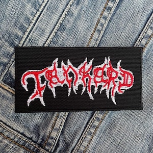 May include: A rectangular black patch with the word "TORKED" embroidered in red and white, featuring a stylized, jagged font. The patch is set against a denim background.