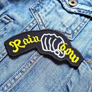 May include: Black and yellow embroidered patch with the word "Rainbow" and a hand pointing to the right.