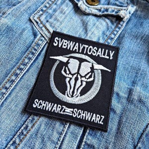 Könnte beinhalten: Schwarz-weiß gestickter Patch mit einem Stierkopf und dem Text "Subway to Sally" und "Schwarz=Schwarz".