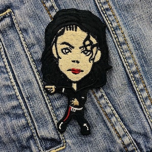May include: Embroidered patch depicting a cartoon of a famous singer in a black outfit with a red stripe. The patch has black hair, red lips, and is set against a denim background. The patch is approximately 7.6 cm tall.