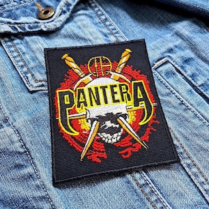 Puede incluir: Parche bordado negro y rojo con la palabra "Pantera" y una calavera con espadas cruzadas.
