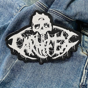 Peut inclure: Patch brodé noir et blanc avec le mot "Darkthrone" dans une police gothique. Le patch présente un crâne avec un motif de crâne.