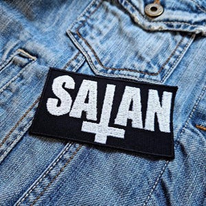 May include: A black and white embroidered patch with the word "SAIAN" and an upside-down cross.
