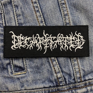 Puede incluir: Parche negro con texto bordado en blanco que dice "DECAPITATED".