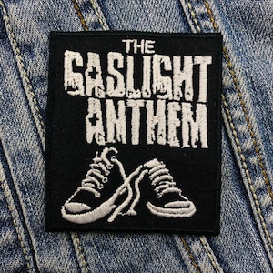 May include: Black and white embroidered patch featuring the text "The Gaslight Anthem" and a pair of white trainers.