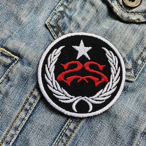 May include: A black and white embroidered patch with a red "2S" logo, a white star, and a white wreath design. The patch is sewn onto a blue denim jacket.