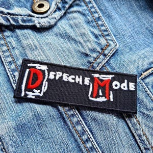 May include: Black and white embroidered patch with the text "Depeche Mode" in white and a red "D" and "M" in the design.