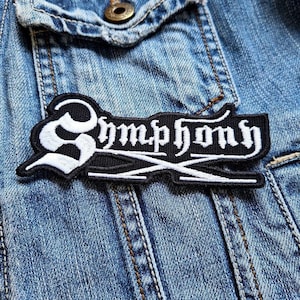 May include: Black and white embroidered patch with the word "Symphony" in a gothic font. The patch is sewn onto a blue denim jacket.