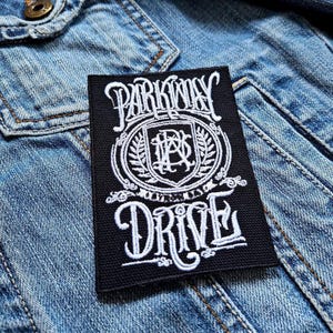 Könnte beinhalten: Schwarz-weiß gestickter Patch mit dem Text "Parkway Drive" und einem Wappen mit den Buchstaben "PD" in einem Kreis.