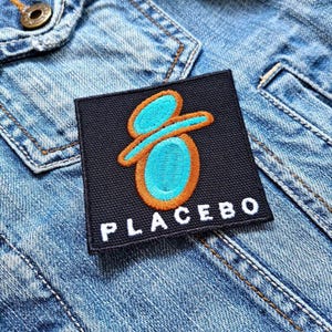 May include: A black fabric patch with a blue and orange stylized graphic and the word "PLACEBO" in white lettering.
