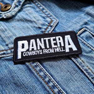 Puede incluir: Parche bordado en blanco y negro con la palabra "PANTERA" y el texto "COWBOYS FROM HELL" en una chaqueta vaquera azul.