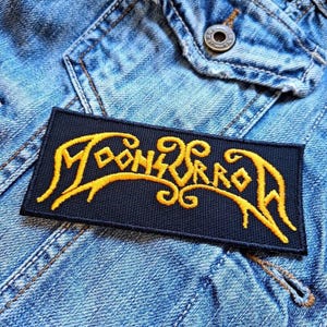 Op de afbeelding: Een zwarte patch met het woord "Moonsorrow" geborduurd in geel.