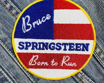 May include: A round, embroidered patch with a red, white, and blue American flag design. The text "Bruce Springsteen Born to Run" is stitched in white on the patch.