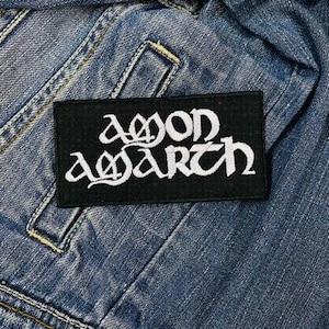 Op de afbeelding: Zwarte patch met witte geborduurde tekst die "Amon Amarth" luidt.