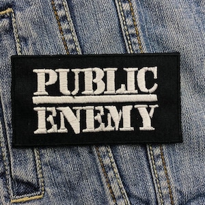 May include: Black and white embroidered patch with the text "PUBLIC ENEMY" on a denim jacket.