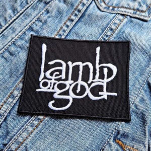 May include: Black and white embroidered patch with the text "Lamb of God" in a stylised font.