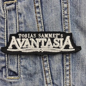 Może przedstawiać: Czarno-biała naszywka haftowana z tekstem "Tobias Sammet's Avantasia" na tle dżinsu.