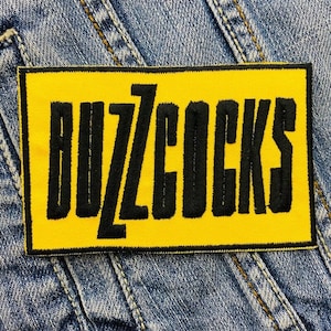 May include: Yellow embroidered patch with the word "BUZZCOCKS" in black lettering.