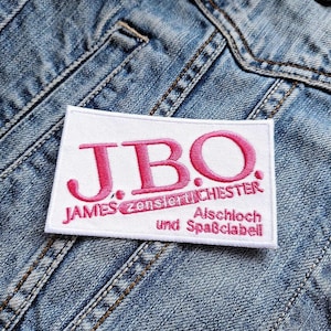 May include: White patch with pink embroidered text that reads "JBO. JAMES zenslertiCHESTEr und Alschloch Spaßclabe".