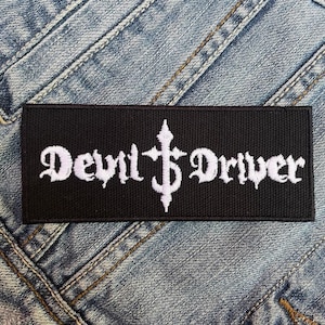 May include: Black embroidered patch with white lettering that reads "Devil Driver" with a stylized cross in between the words.