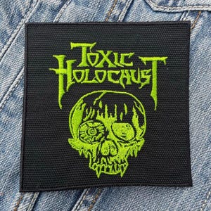 Könnte beinhalten: Grüner gestickter Patch mit dem Text "Toxic Holocaust" und einem grünen Schädel mit einem Auge.