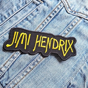 May include: A black and yellow embroidered patch with the text "Jimi Hendrix" on a denim jacket.