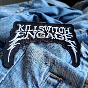 May include: Black and white embroidered patch with the text "Killswitch Engage" on a denim jacket.