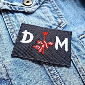 May include: A black patch with white letters that spell "D.O.M." and a red stylized flower in the middle.