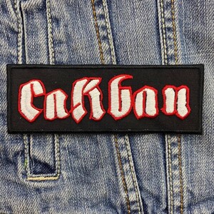 Puede incluir: Parche bordado negro con la palabra "Carbon" en letras blancas con contornos rojos. El parche está sobre un fondo de mezclilla.