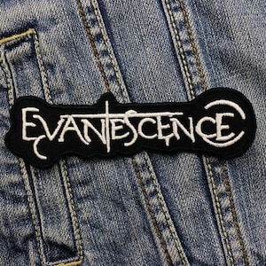 Könnte beinhalten: Schwarz-weiß gestickter Patch mit dem Wort "EVANESCENCE" in einer stilisierten Schrift.