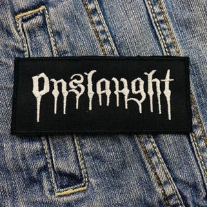 May include: A black rectangular patch featuring the word "Pnslarght" in white gothic script. The patch is displayed on a blue denim background, highlighting the fabric's texture and stitching.