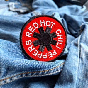 May include: Red Hot Chili Peppers band logo patch with a red background and white text. The logo features a black star with four points.