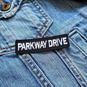 Könnte beinhalten: Ein schwarz-weißes Patch mit dem Text "Parkway Drive" auf einer blauen Jeansjacke.