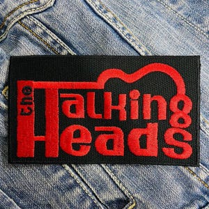 May include: Black fabric patch with red embroidered text that reads "The Talking Heads".