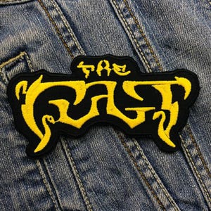 May include: A black and yellow embroidered patch with the text "The Gas" in a stylized font.