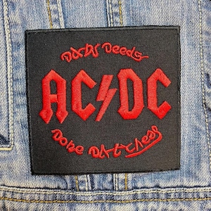 Op de afbeelding: Zwart vierkantige patch met rode geborduurde tekst en logo. De tekst luidt "Dirty Deeds Done Dirt Cheap" met de bandnaam "AC/DC" in het midden. De patch is op een spijkerjas genaaid.