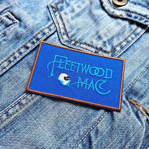 May include: Blue and white embroidered patch with the text "Fleetwood Mac" on a denim jacket.