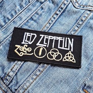 Op de afbeelding: Zwart-witte geborduurde patch met de tekst "LED ZEPPELIN" en vier symbolen. De symbolen zijn een gestileerde "Zoso", een cirkel met een verticale lijn, een cirkel met drie in elkaar grijpende cirkels en een driehoek met een cirkel erin.