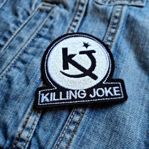 May include: A black and white embroidered patch with the letters "KJ" in a circle and the words "KILLING JOKE" below.