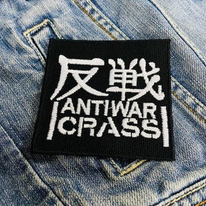 Peut inclure: Patch noir avec du texte blanc qui dit "反戦" et "ANTIWAr CRASS".