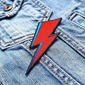 Könnte beinhalten: Roter und blauer Blitz-Patch auf einer Jeansjacke.
