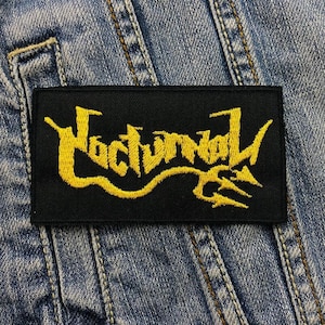 May include: Black and yellow embroidered patch with the word "Nocturnal" in a stylised font.