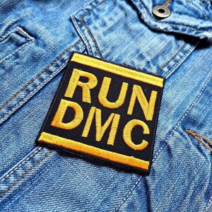 May include: A black and yellow embroidered patch with the text "RUN DMC" on a blue denim jacket.