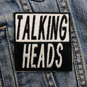 Op de afbeelding: Zwart-witte geborduurde patch met de tekst "TALKING HEADS" in witte letters op een zwarte achtergrond.