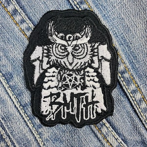 Puede incluir: Parche bordado en blanco y negro con un diseño de búho, un pentagrama y texto estilizado. El parche está sobre un fondo de mezclilla. El búho tiene patrones de plumas detallados y un pico prominente.